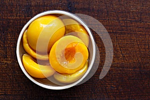 Canned peach halves in bowl isolated on dark background. From ab