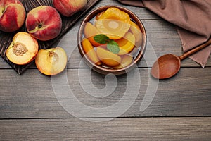 Canned peach halves in bowl on wooden table, flat lay. Space for text