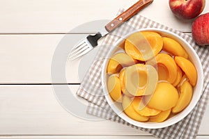 Canned peach halves and fork on white wooden table, flat lay. Space for text