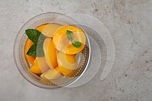 Canned peach halves in glass bowl on light grey table, top view. Space for text