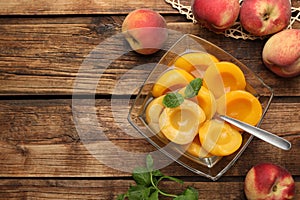 Canned peach halves in glass bowl on wooden table, flat lay. Space for text