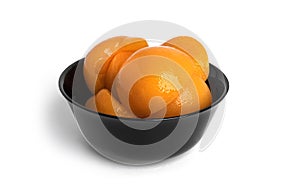 Canned peaches in a black bowl. Sweet peaches in syrup isolated on white background.