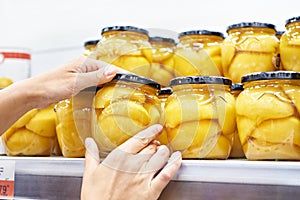 Canned peaches in glass jar in the hands in store