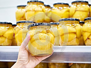 Canned peaches in glass jar in the hands in store