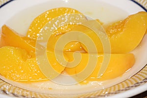 Canned peaches halves sprinkled with syrup in white plate