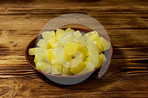 Canned pineapple pieces in ceramic plate on wooden table