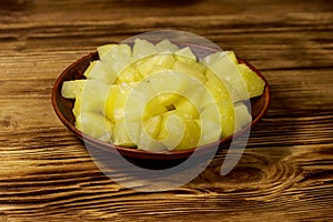 Canned pineapple pieces in ceramic plate on wooden table