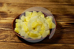 Canned pineapple pieces in ceramic plate on wooden table