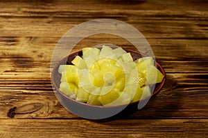 Canned pineapple pieces in ceramic plate on wooden table