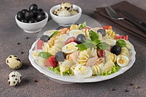 Canned salmon salad with pasta, cherry tomatoes, quail eggs, basil and black olives on brown background, Close-up