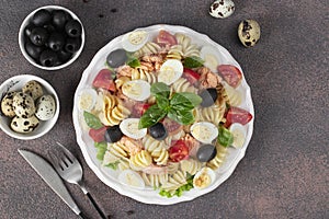 Canned salmon salad with pasta, cherry tomatoes, quail eggs, basil and black olives on brown background, Copy space