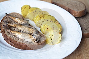 Canned sprats on rye bread served with herb baked potatoes