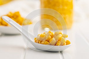 Canned sweet corn on ceramic spoon on white table
