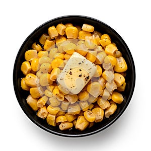 Canned sweet corn with a knob of butter and ground black pepper in a black ceramic bowl isolated on white. Top view