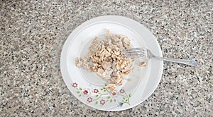 Canned tuna is in a porcelain plate and there is a fork. Close up