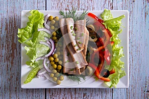 Canned tuna slices with fresh vegetables on white plate on wooden background flat lay, top view
