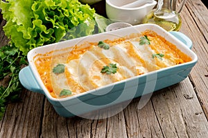 Cannelloni with filling of ground beef, tomatoes, baked with bechamel tomato sauce, side view, old dark wooden background