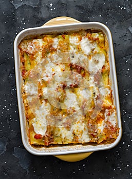 Cannelloni with spinach and ricotta baked with mozzarella in a baking dish on a dark background, top view