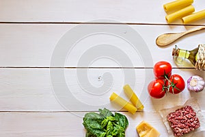 Cannelloni, tomatoes, minced meat and other ingredients. White wooden background. Italian cuisine