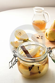 Canning pears with cinnamon and cloves in a glass jar to preserve summer fruits also in winter, white painted table, copy space,