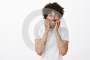 Cannot wait to have bite. Portrait of nervous emotive young man with dark skin and curly hair, biting fingernails from