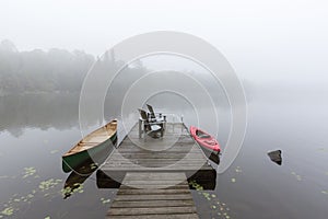 Canoe and kayak tied to a dock on a misty lake - Ontario, Canada