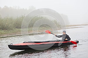 Canoe on lake with beautiful bushes on background. Foggy panorama with male paddler padding on cold water, man canoeing alone,