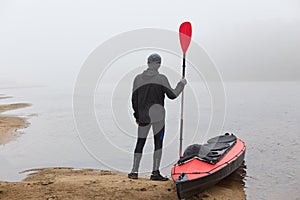 Canoe tour on a river, sportsman posing backwards with oar near red boat, man looking at foggy water, wants rowing boat, enjoying
