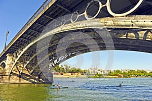 Canoeists sailing under the Triana Bridge on the Guadalquivir River in Seville Spain
