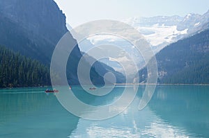 Canoeists traversing the azure waters of Lake Louise, Canada with snow-capped mountains as a backdrop