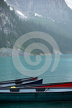 Canoes in turquoise Lake Louise with misty mountains in the background