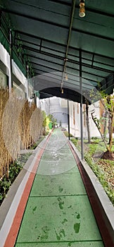 The canopy that protects the open corridor in the garden is surrounded by plants with concrete floors.
