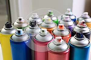 Cans of different graffiti spray paints on blurred background, closeup