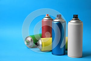 Cans of different graffiti spray paints on light blue background, space for text