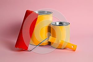 Cans of orange paint and roller on pink background