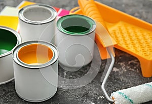 Cans of paint, roller and brush on grey background