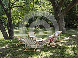 Canvas chair and wooden table under the tree in garden. Afternoon tea party setup.