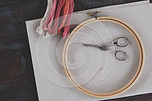 Canvas for embroidery with a cross embroidered in a round wooden hoop, multi-colored thread mouline thread, needle