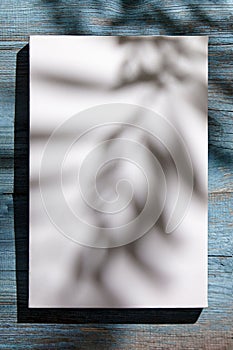 Canvas mockup, white blank picture hanging on blue wooden wall with dark shadows of palm leaves. Poster mock up, empty canvas with