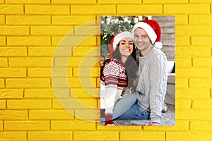 Canvas with printed photo happy couple wearing Santa hats on yellow brick wall, space for text