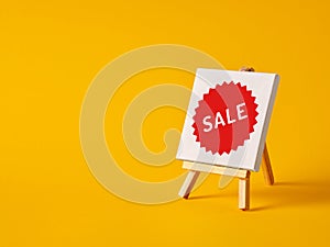 A canvas with the word sale on an easel with yellow background with copy space