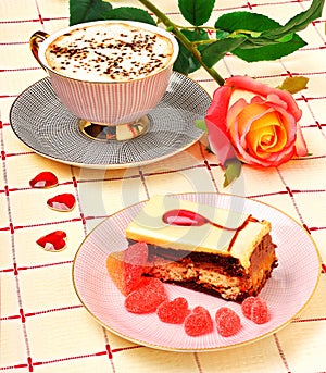 Cap of coffee, a rose and a cake on tablecloth