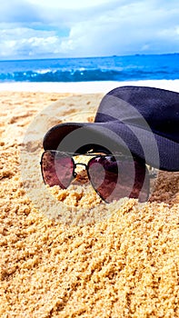 Cap placed on top of a sunglasses on the beach sand with the blue sea and the sky with clouds in the background. photo