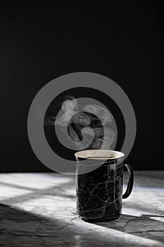 The cap of hot coffee with steam on the marble table