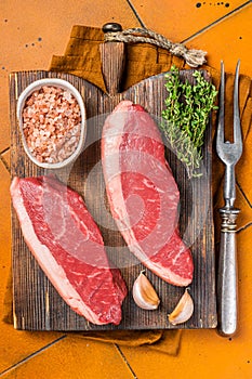 Cap Rump steak, raw beef meat steak with thyme and salt on wooden butcher board. Orange background. Top view