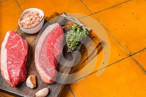 Cap Rump steak, raw beef meat steak with thyme and salt on wooden butcher board. Orange background. Top view. Copy space