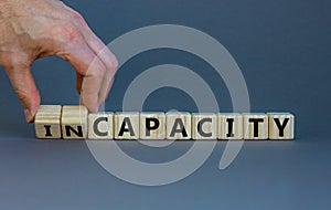 Capacity or incapacity symbol. Businessman turns wooden cubes and changes the word `incapacity` to `capacity`. Beautiful grey