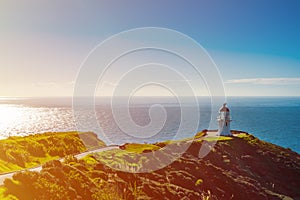 Cape Reinga Lighthouse in evening sunlight, azure surface of calm ocean behind. Famous tourist attraction at Cape Reinga