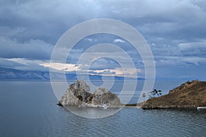 Cape Shamanka rock in clear Lake Baikal among mountains and clouds photo