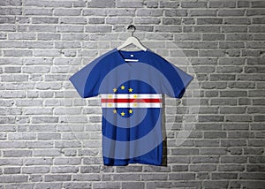 Cape Verde flag on shirt and hanging on the wall with brick pattern wallpaper photo